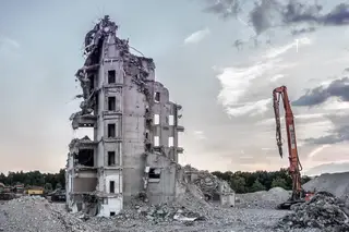 A partially demolished concrete apartment block with a high-reach excavator arm at dusk.